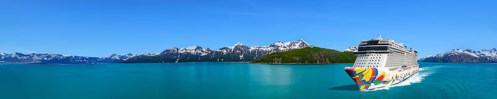 A colorfully decorated cruise ship sailing through turquoise waters with snow-capped mountain