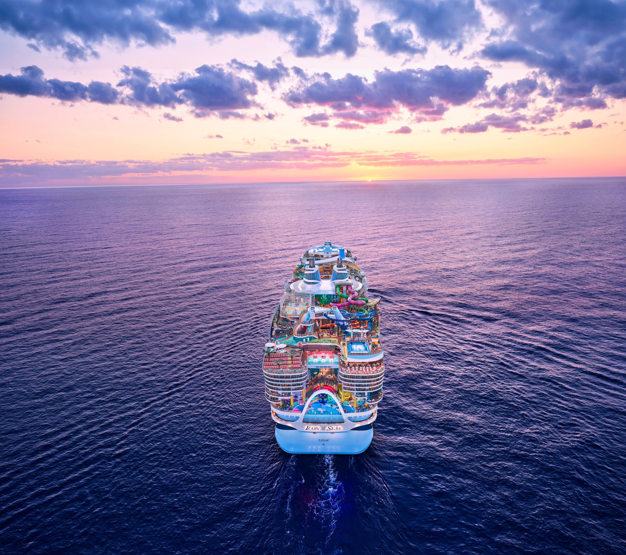An aerial photograph of a massive modern cruise ship sailing on calm ocean waters during a dramatic