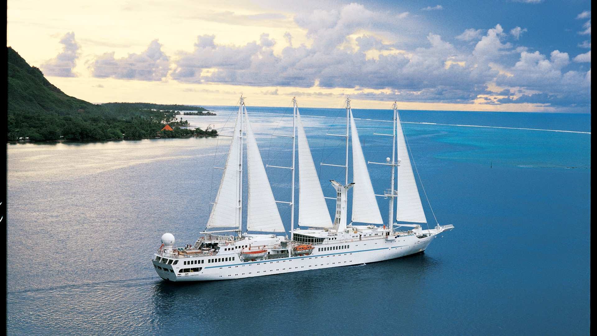 A luxurious four-masted sailing cruise ship with white sails fully deployed, anchored