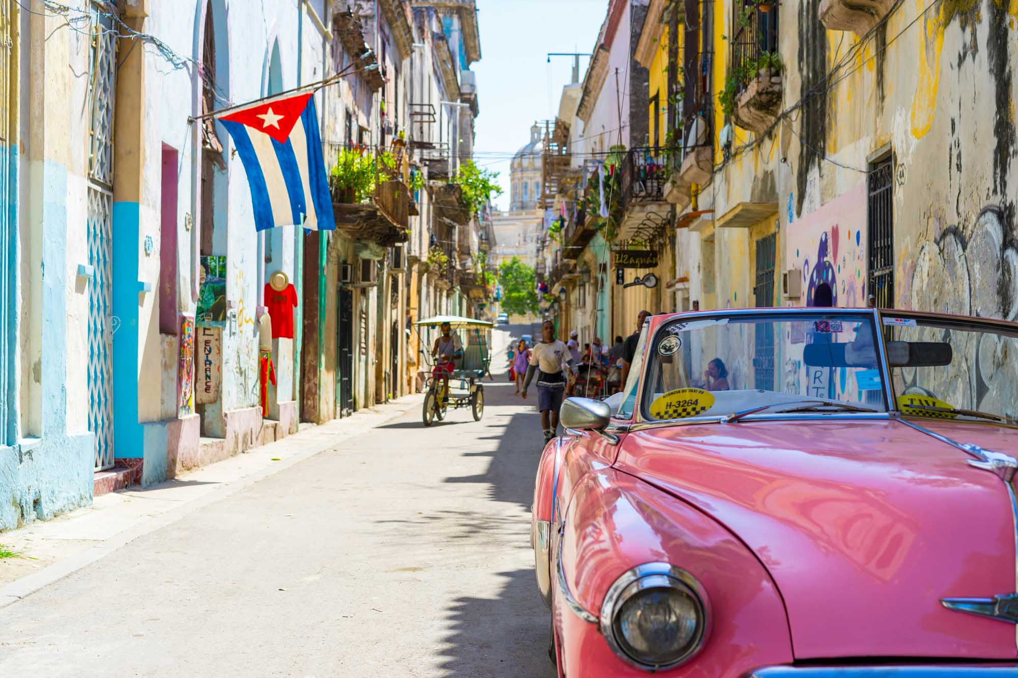 A vibrant street scene in Havana, Cuba featuring a pink vintage American car parked along