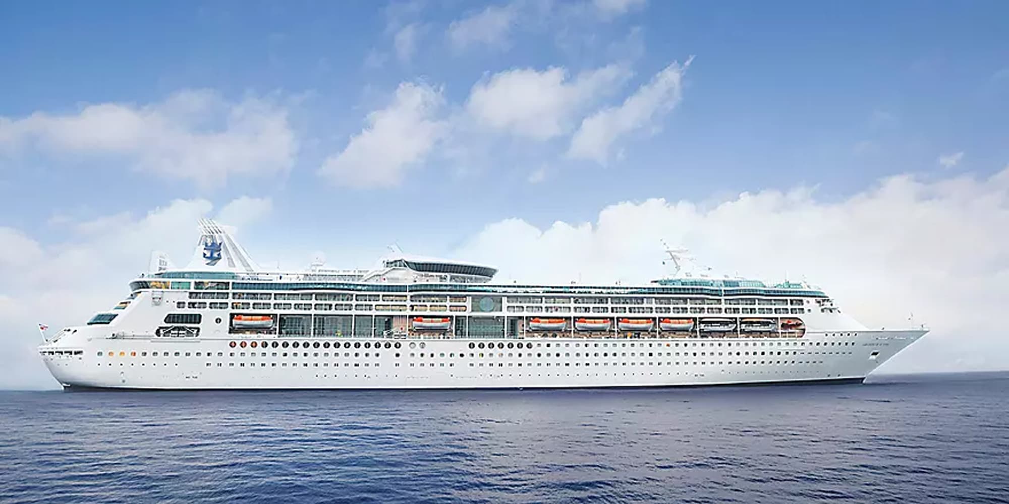 A large white cruise ship with turquoise accents sails through calm blue waters under a partly