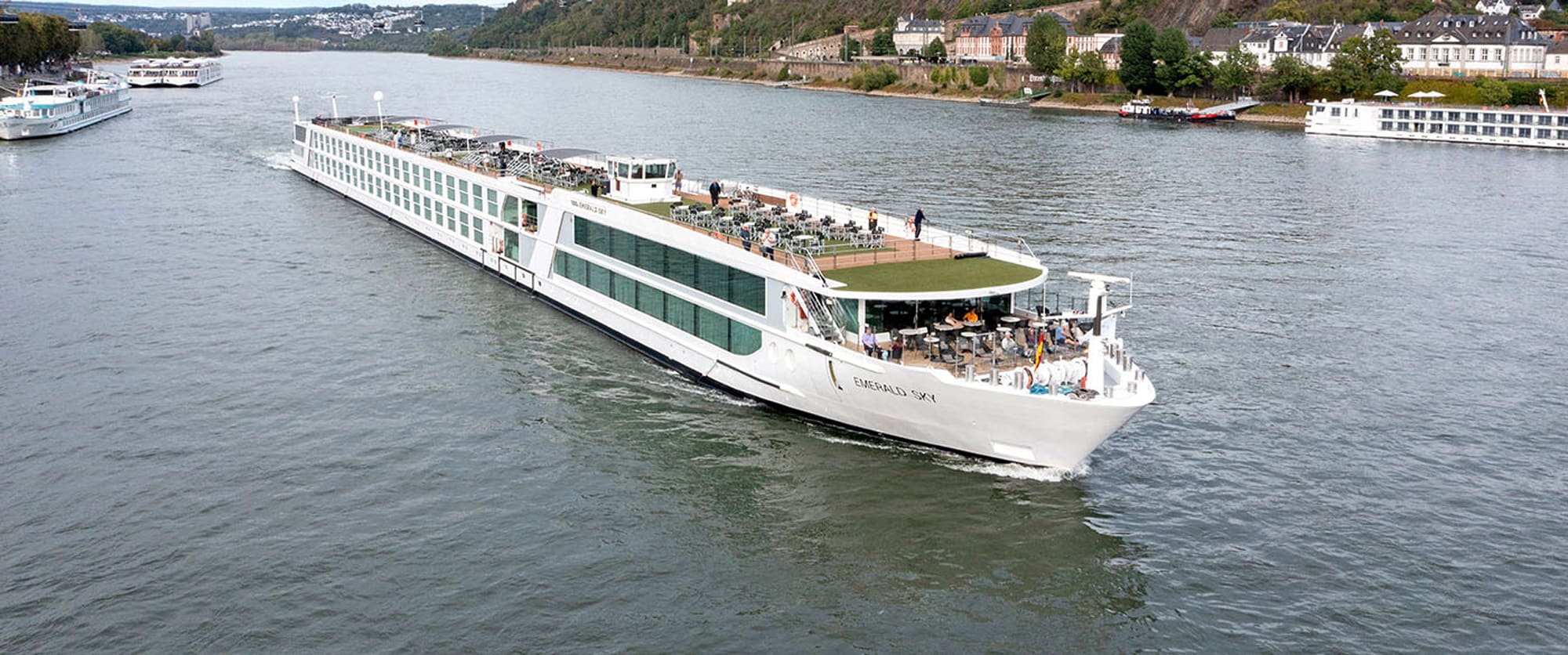 A modern white river cruise ship sailing along a scenic river with historic buildings and landscape
