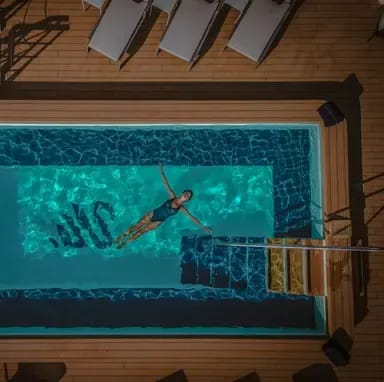 An overhead view of a snorkeler in vibrant turquoise water near a wooden deck with lounge chairs