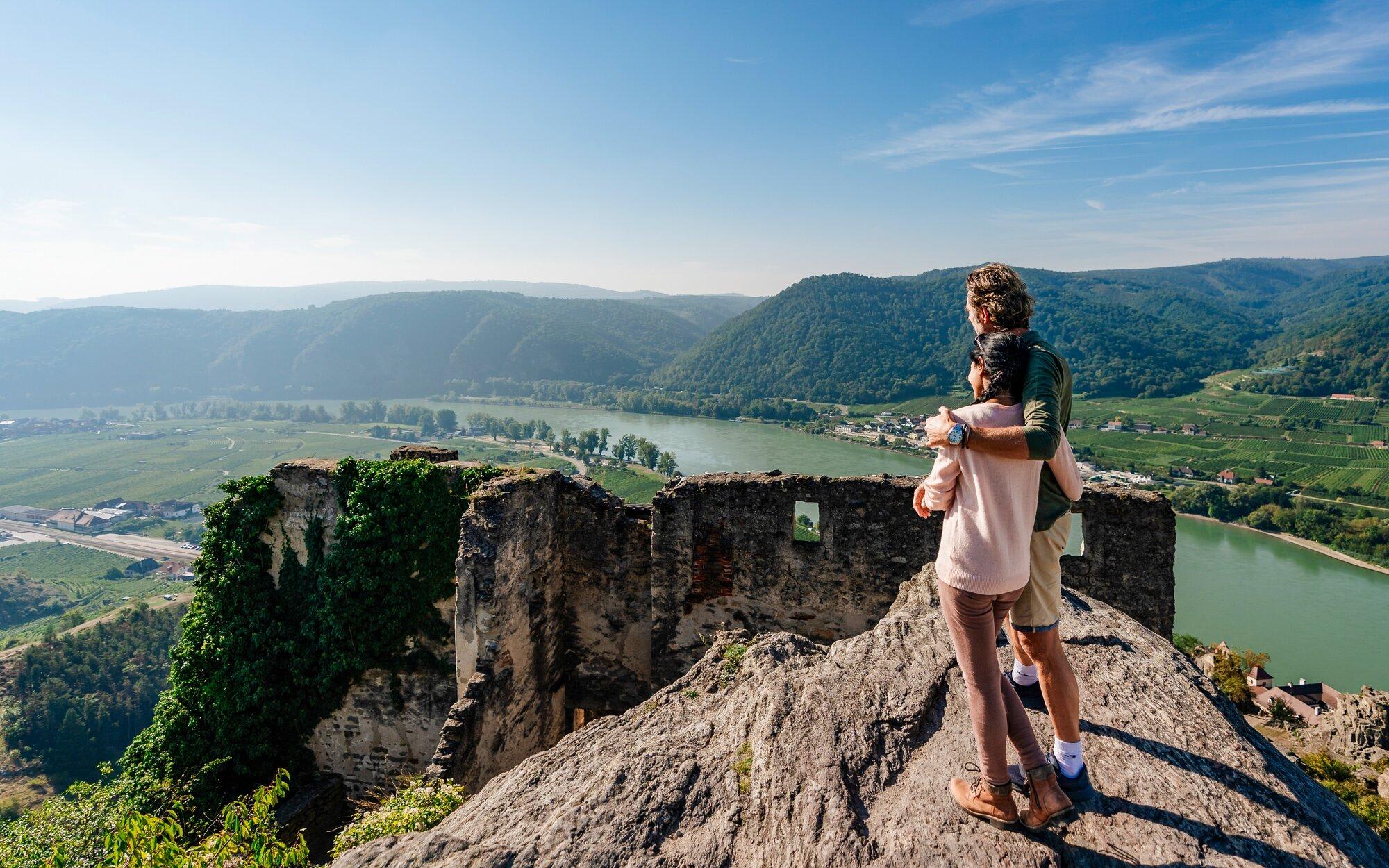 An adult hiker carrying a young child stands atop the ruins of Dürnstein Castle, overlooking