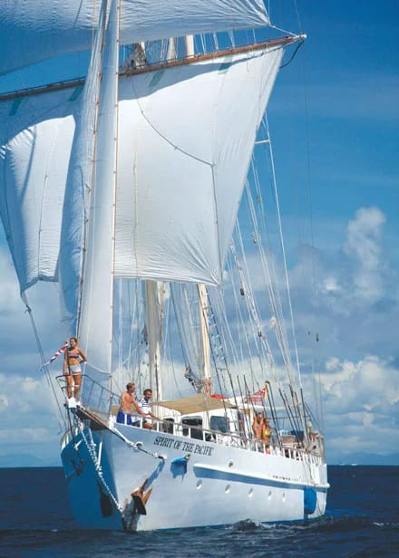 A stunning tall ship with white sails fully deployed against a brilliant blue sky with scattered clouds, featuring multiple crew members visible on deck. The vessel 'Spirit of the Sea' displays traditional sailing characteristics with multiple masts and rigging, captured during optimal sailing conditions on calm waters.