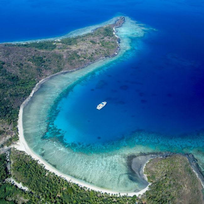 An aerial view of a pristine tropical island featuring a crescent-shaped white sand beach