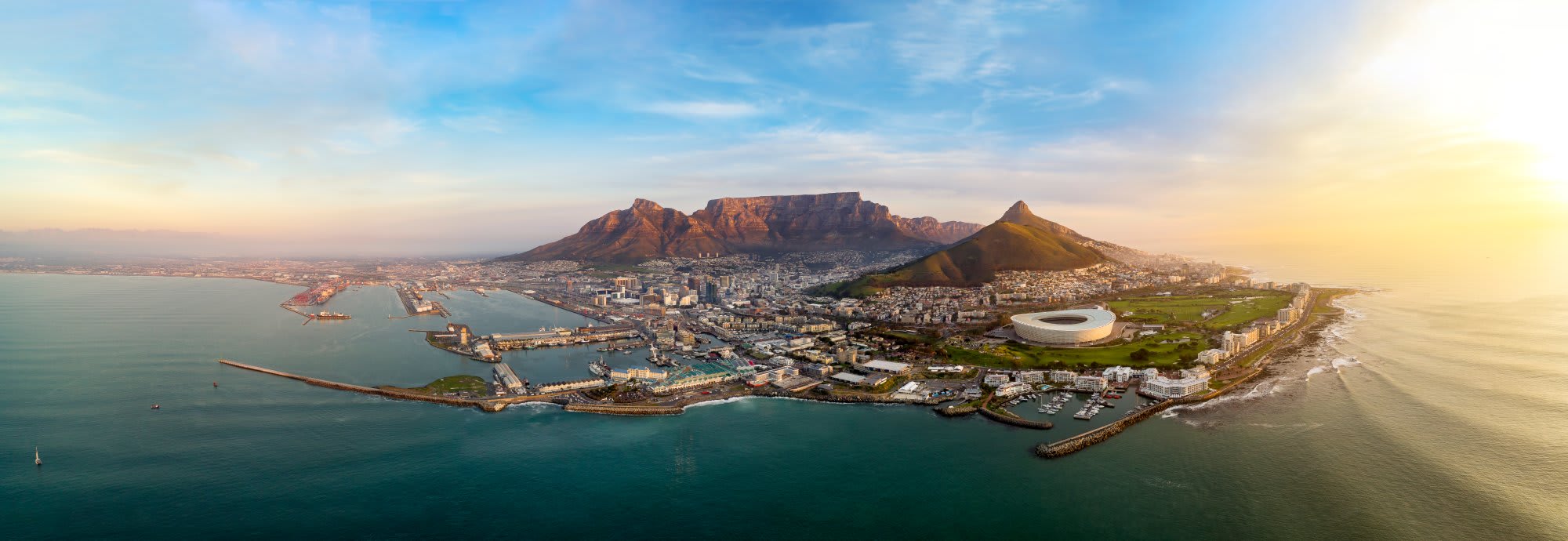 An expansive aerial photograph of Cape Town, South Africa at sunset, showcasing Table Mountain