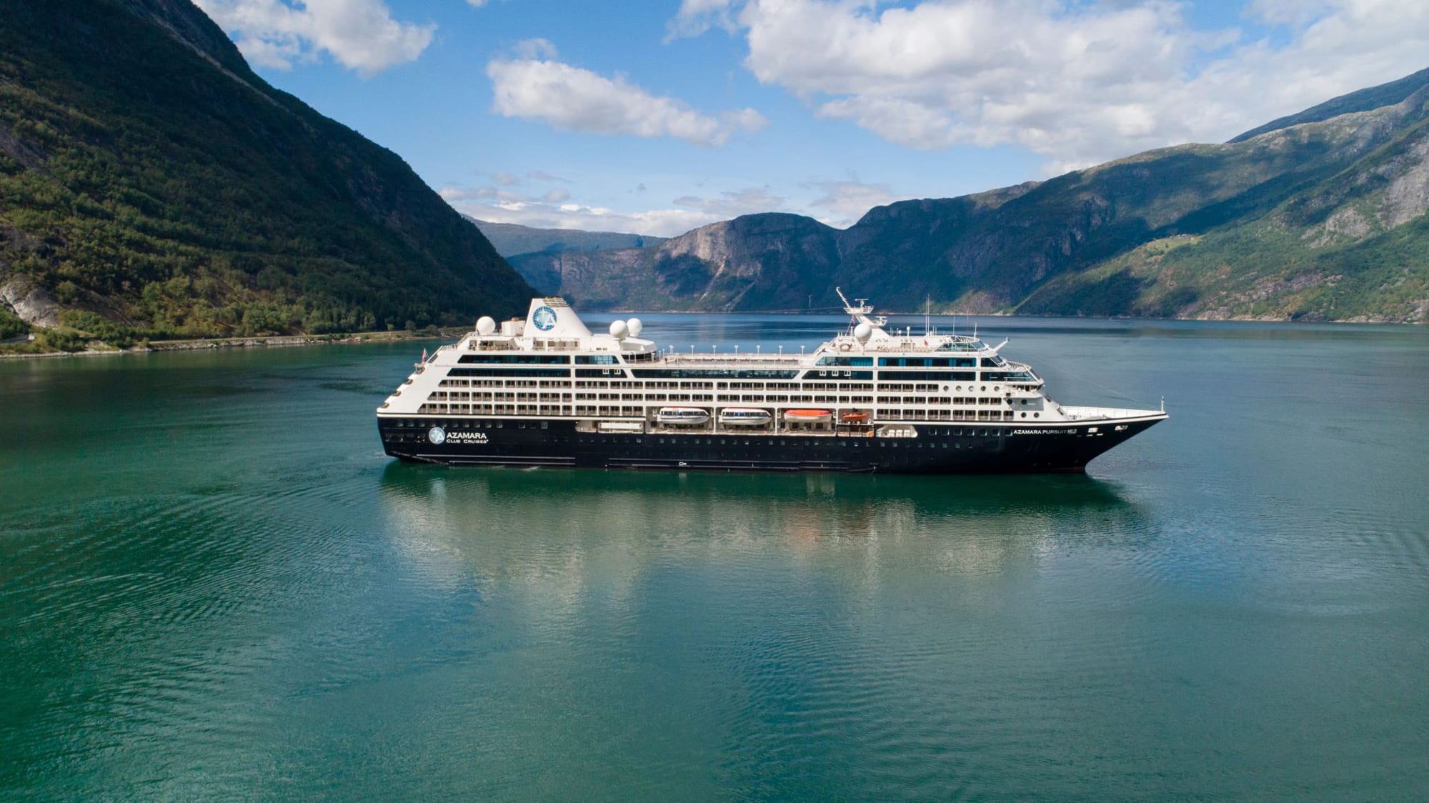 A large modern cruise ship anchored in a stunning Norwegian fjord, surrounded by steep mountains