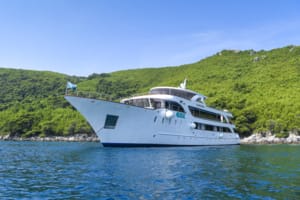 A sophisticated white multi-deck motor yacht is anchored in crystal-clear turquoise waters adjacent