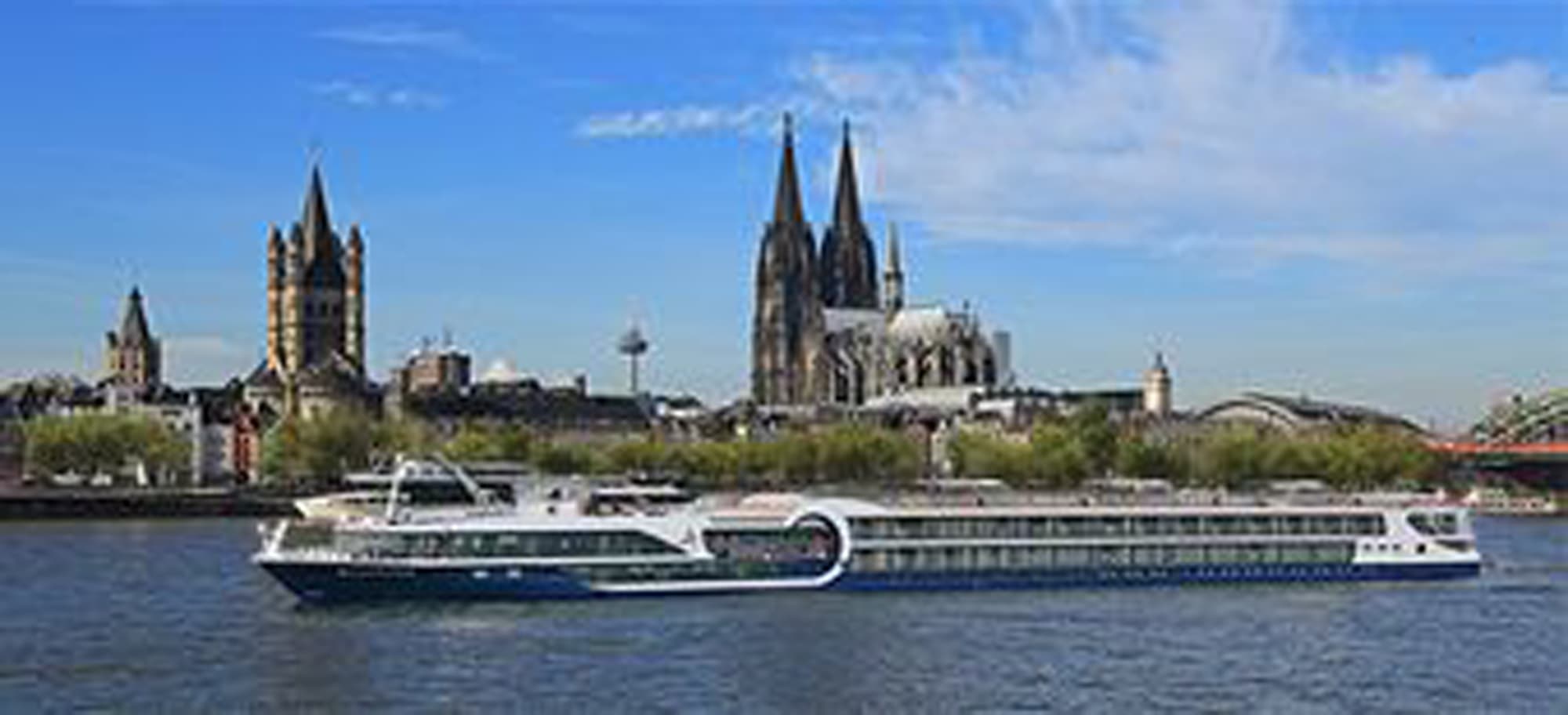 A modern river cruise ship navigates the Rhine River with the iconic Cologne Cathedral