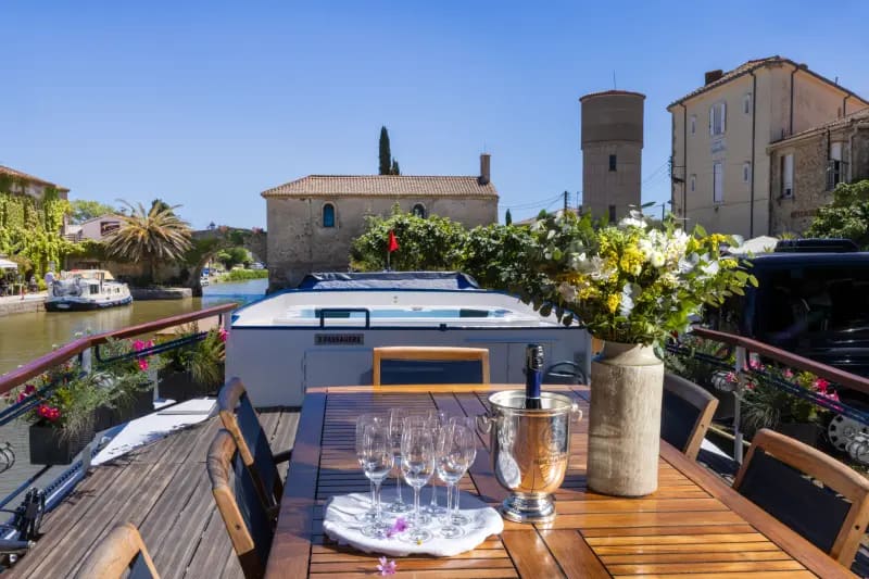 An elegant outdoor dining setup on the deck of a luxury river barge moored along a scenic European