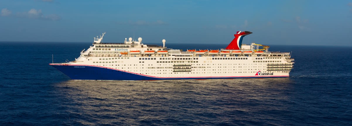 A large white Carnival cruise ship sailing on blue ocean waters with a clear sky background. The vessel displays the distinctive red Carnival funnel and appears to be mid-voyage.