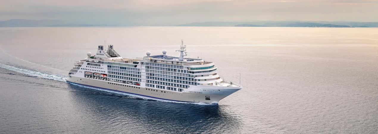 A large, white multi-deck cruise ship sailing across a calm, expansive ocean with soft pastel sky