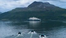 A white cruise ship anchors in pristine blue-green waters surrounded by snow-capped mountains