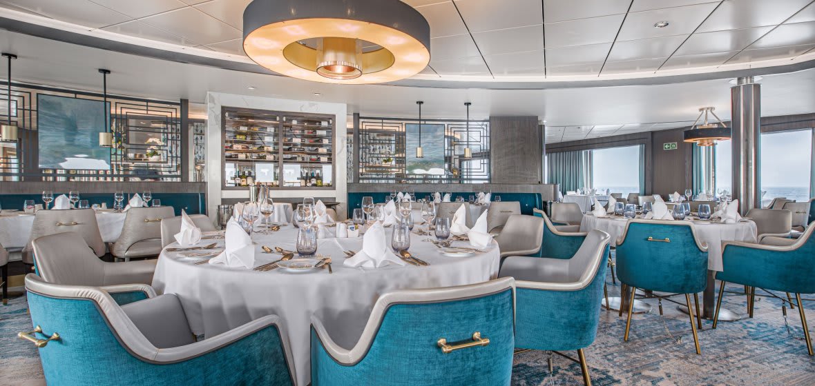 A sophisticated cruise ship dining venue featuring round tables dressed in white linens, modern