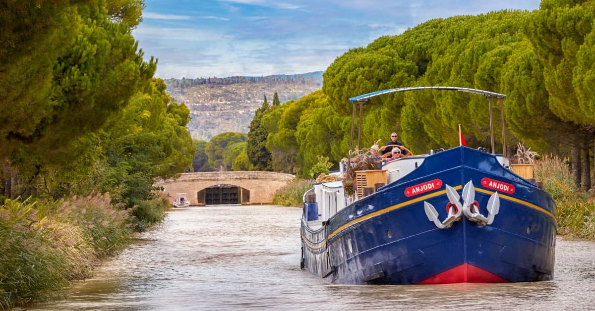 A traditional blue and gold barge named Anjobi navigates through a historic stone canal lock in