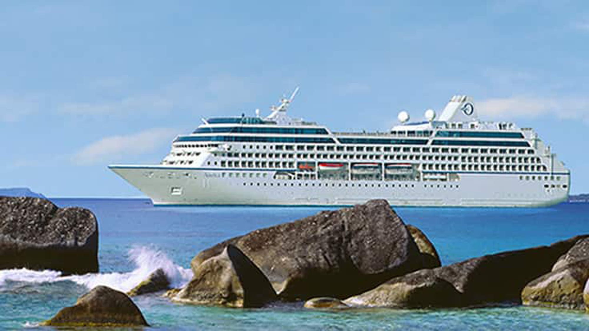 A white and blue cruise ship sailing on turquoise waters near large rocky formations in