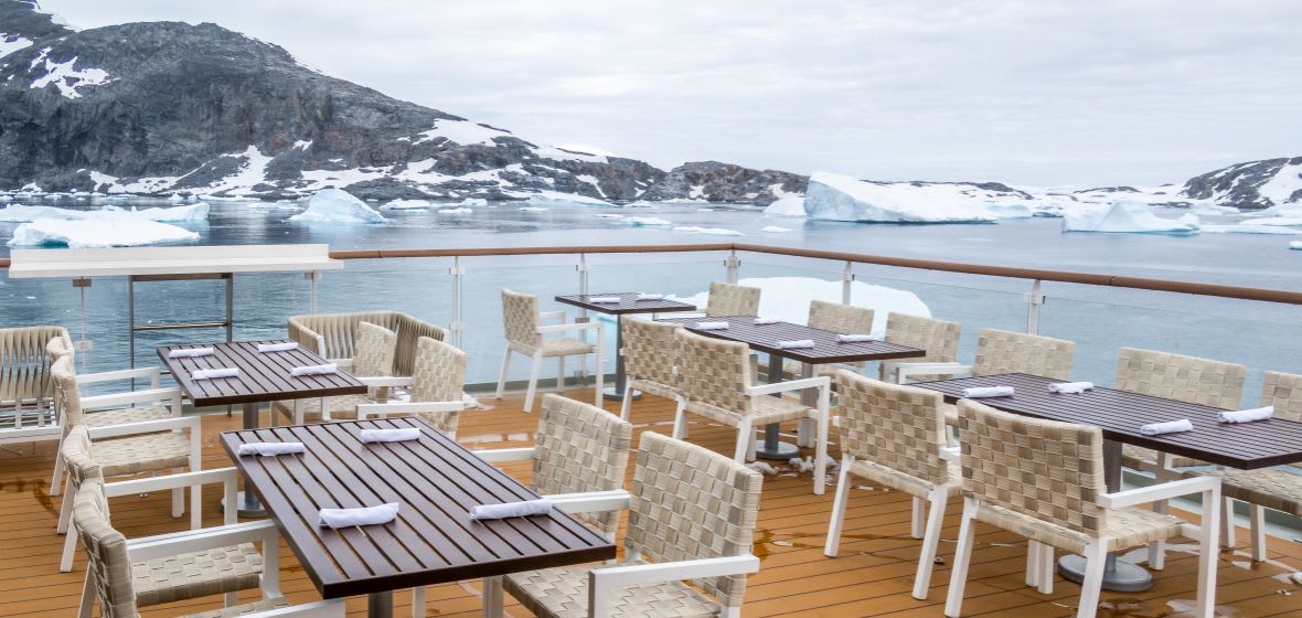 An elegant outdoor dining and lounge area aboard a cruise ship overlooking a pristine Arctic