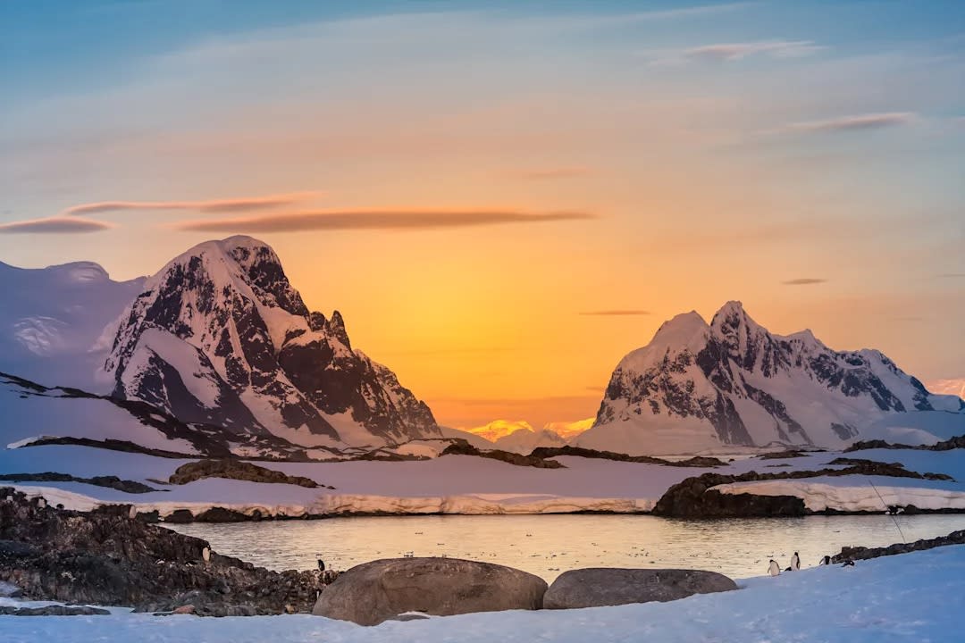 A breathtaking polar landscape featuring towering snow-covered mountain peaks framed by golden
