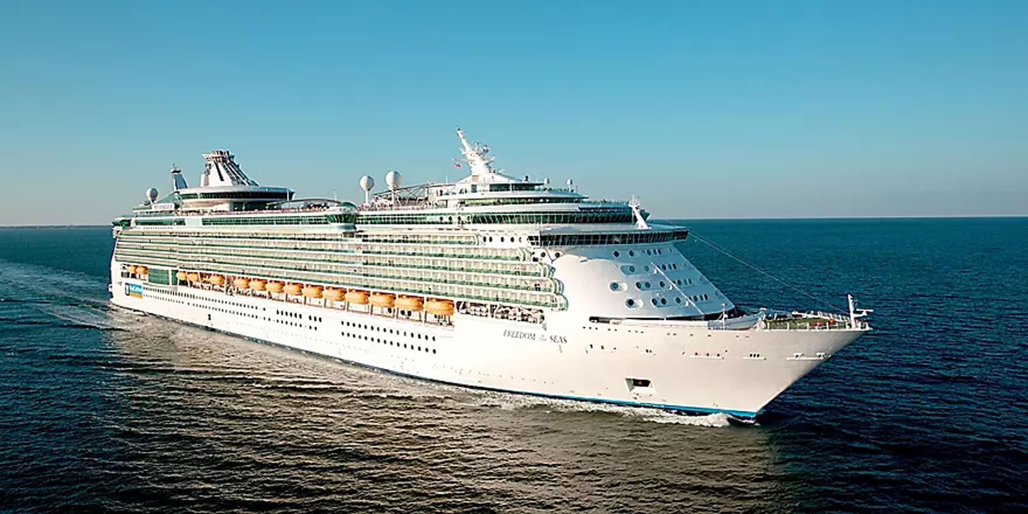 A large modern cruise ship photographed from an aerial perspective sailing on turquoise blue waters