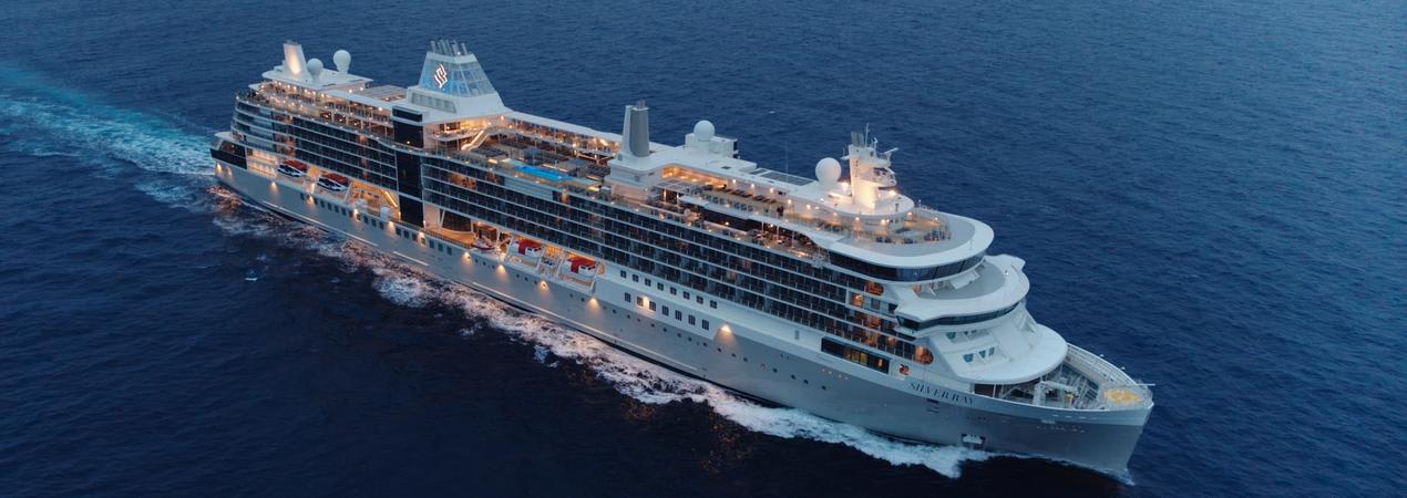 A sleek, illuminated cruise ship navigating through deep blue waters, showcasing multiple decks