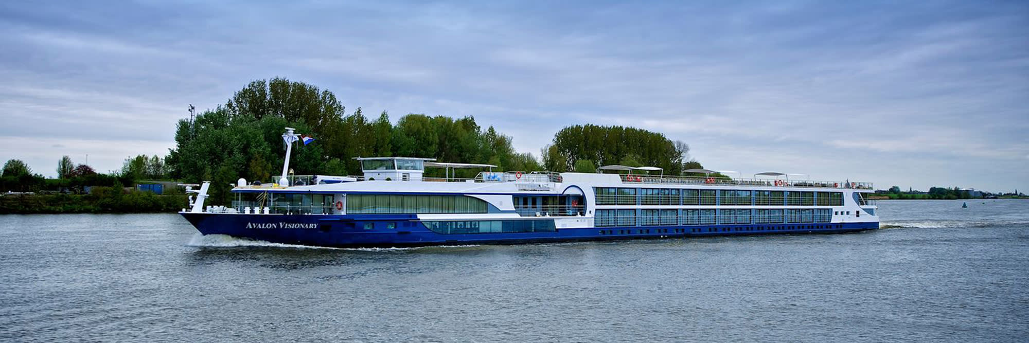 The Avalon Visionary, a modern river cruise ship, sails through a scenic waterway lined with lush