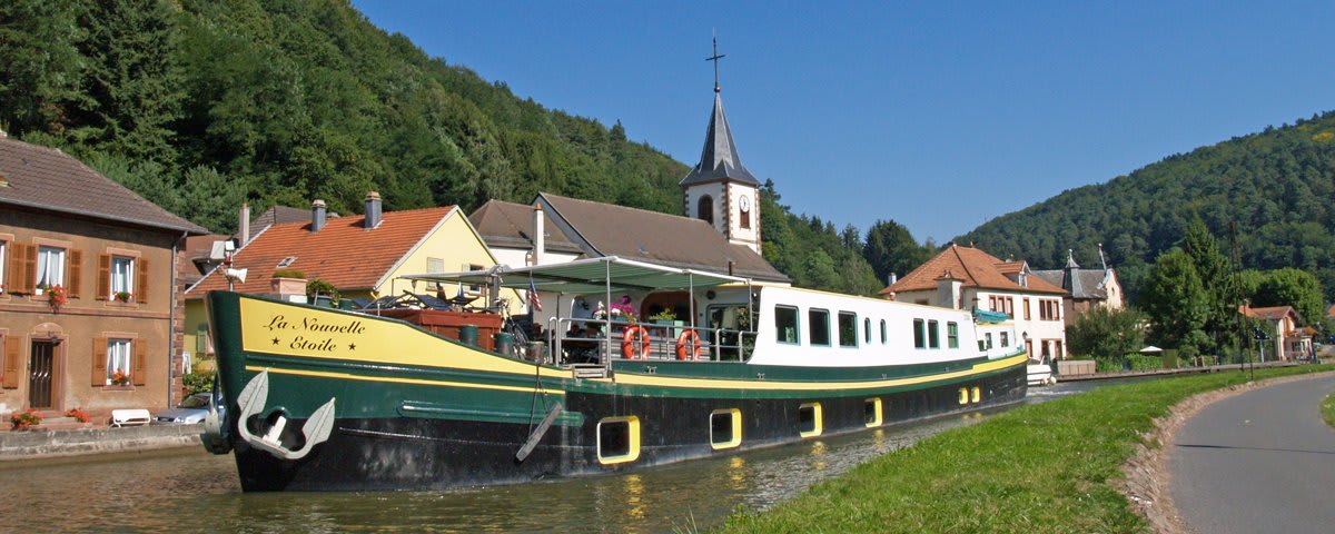 A traditional green and yellow canal barge named 'La Nouvelle Étoile' navigates through