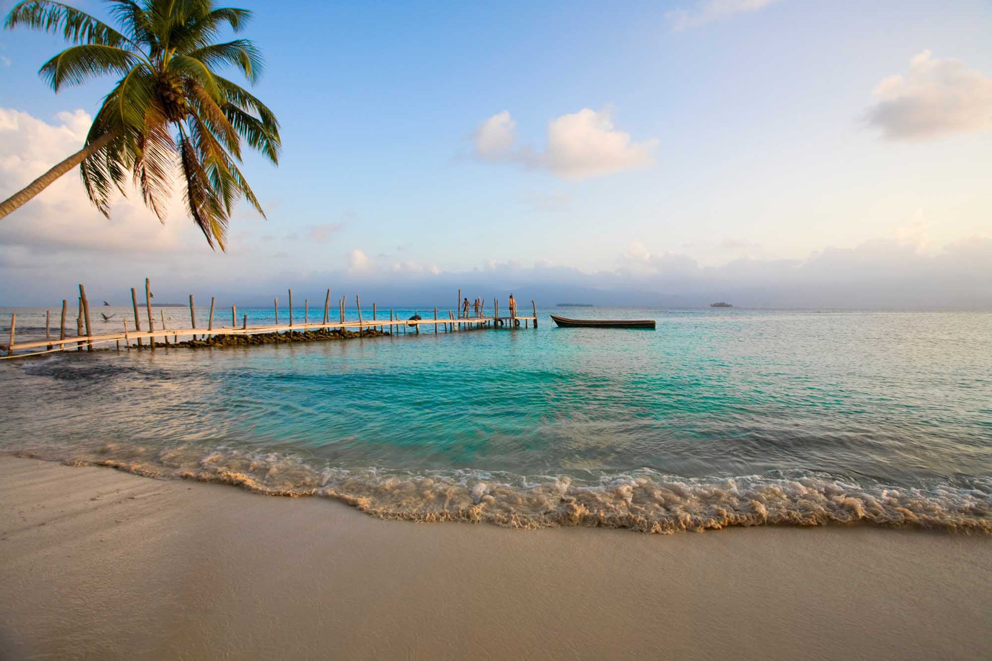A pristine tropical beach scene featuring turquoise waters, white sand, and a traditional wooden