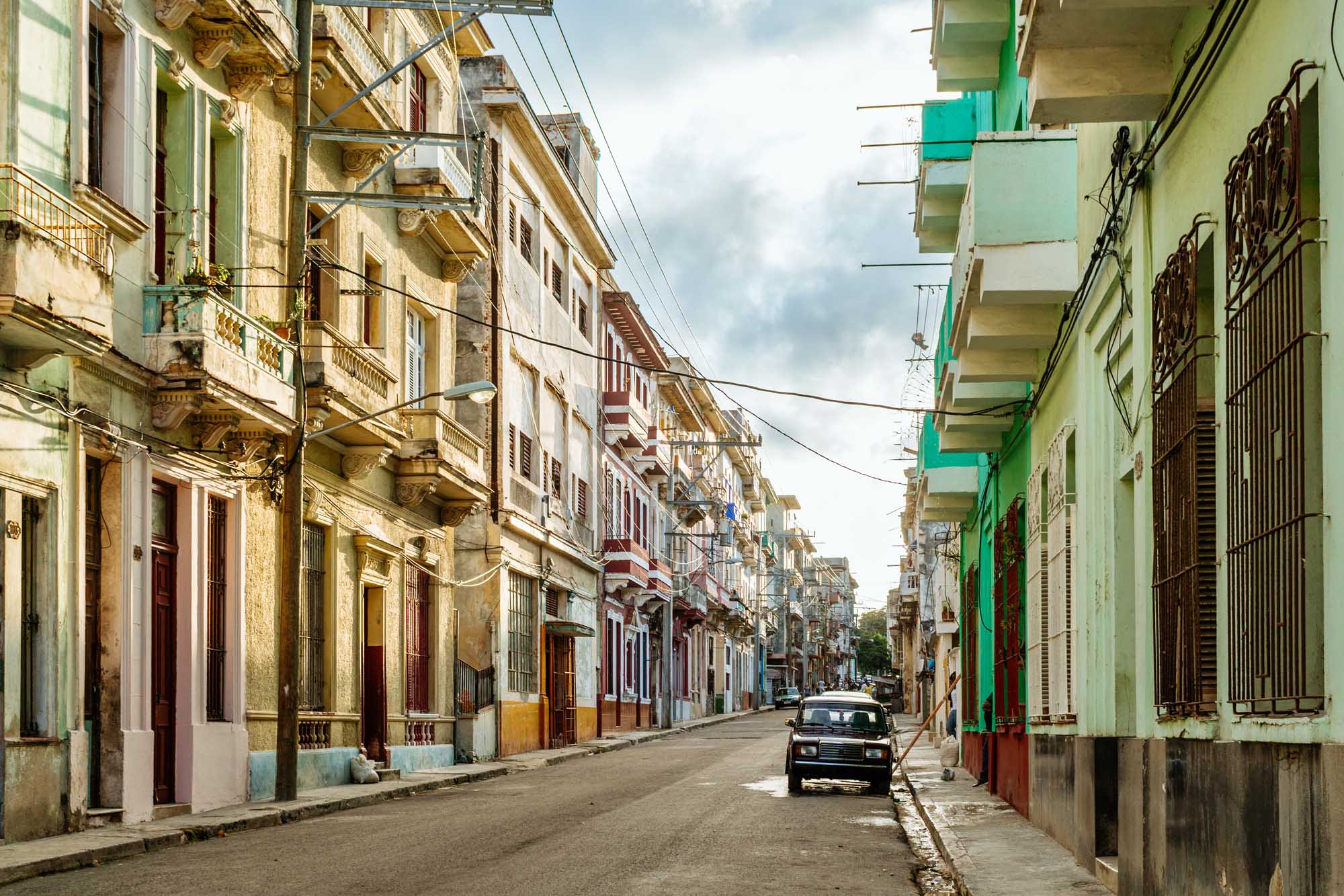 A vibrant street scene in historic Havana lined with pastel-colored colonial buildings featuring