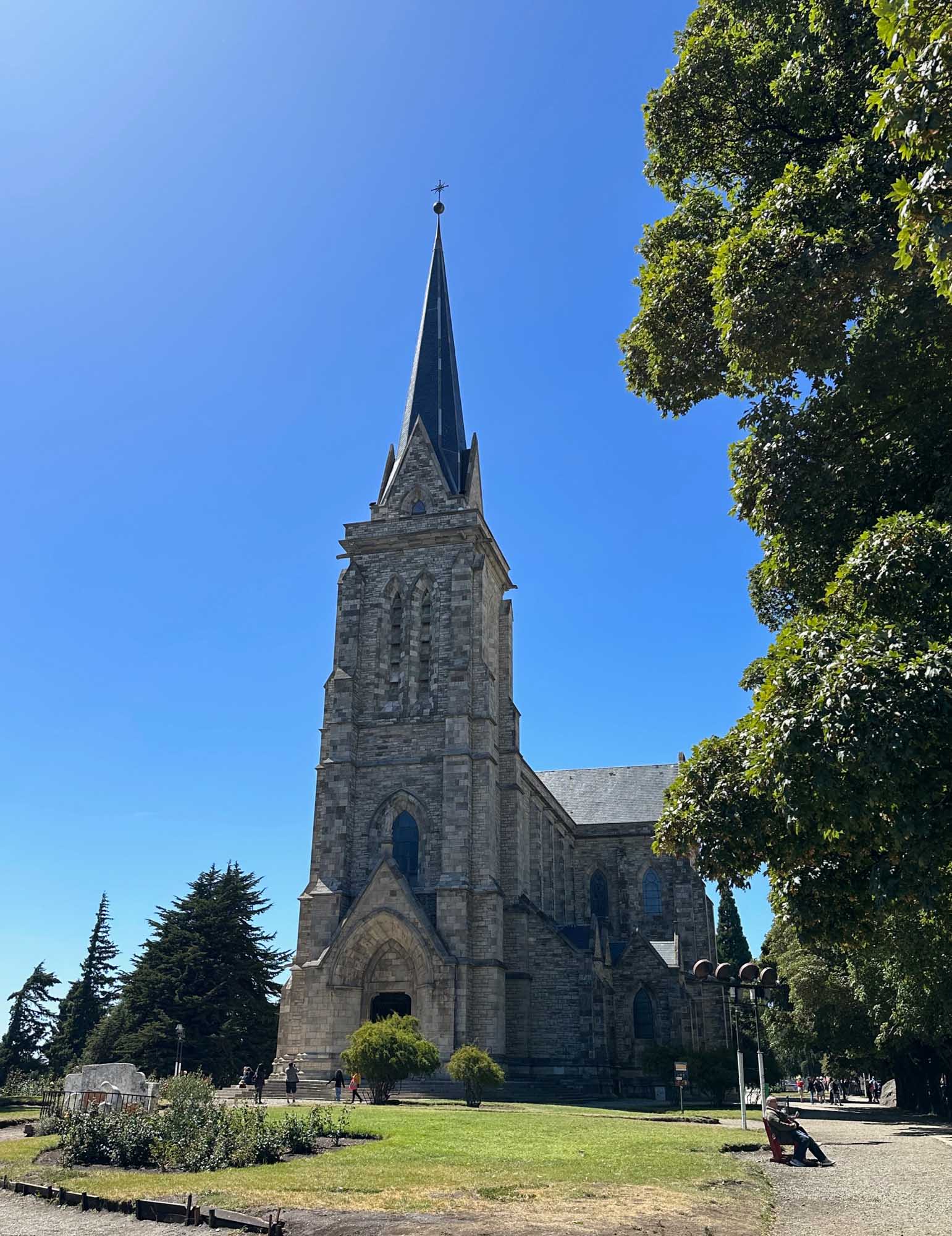 A striking Gothic Revival stone church with a tall pointed spire topped by a cross stands