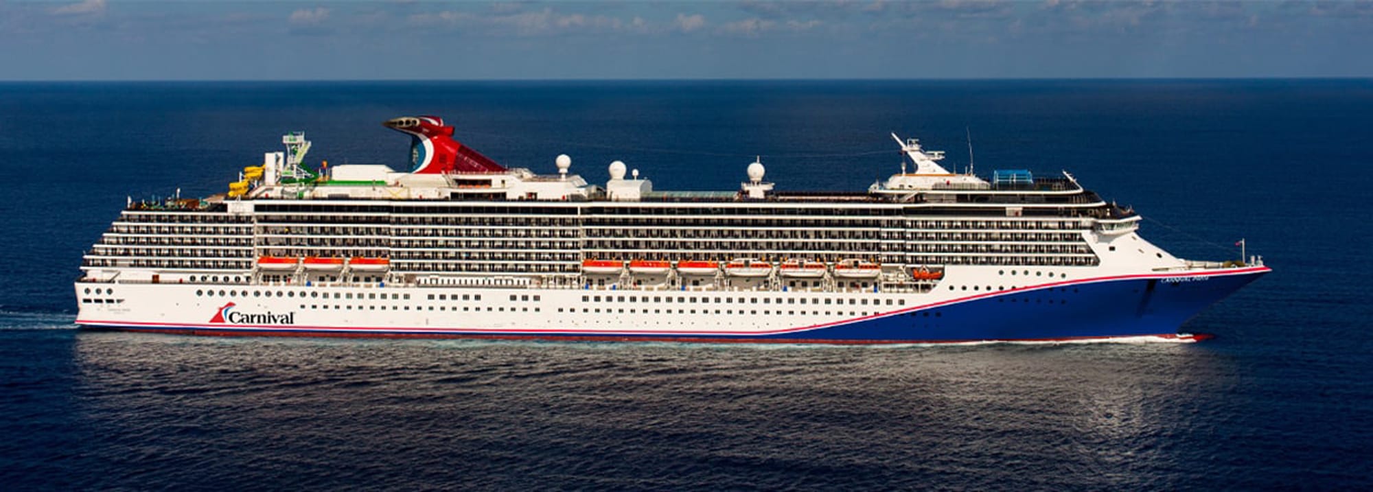 A large white and red Carnival cruise ship sailing on open blue waters, showcasing the vessel's