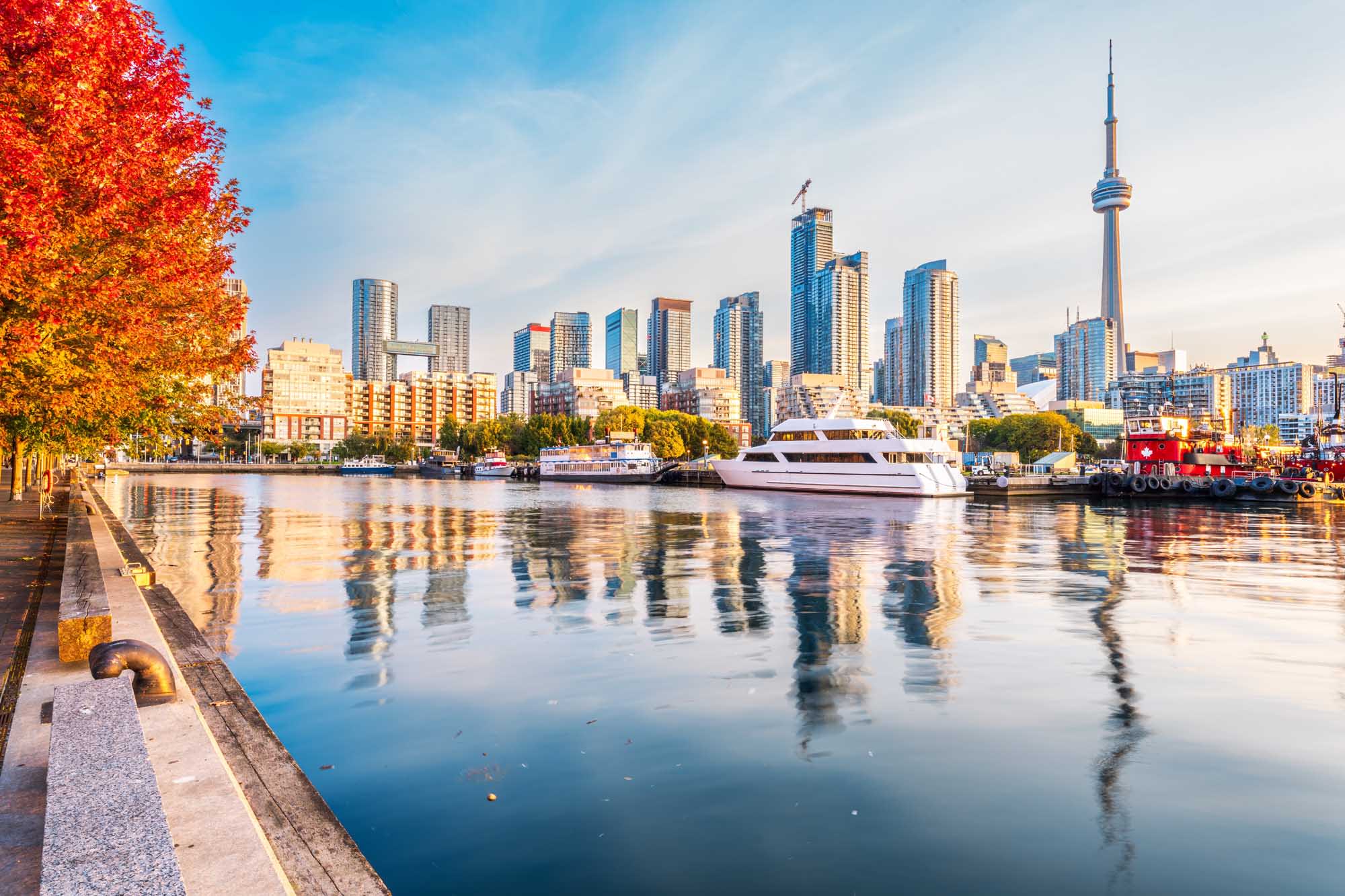 A stunning autumn view of Toronto's iconic skyline reflected in still waterfront waters, featuring