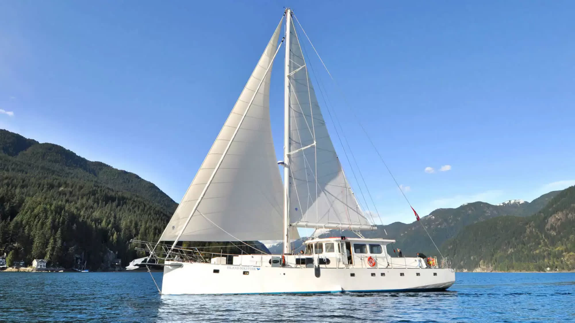 A stunning white sailing catamaran with full sails deployed on a pristine alpine lake, surrounded