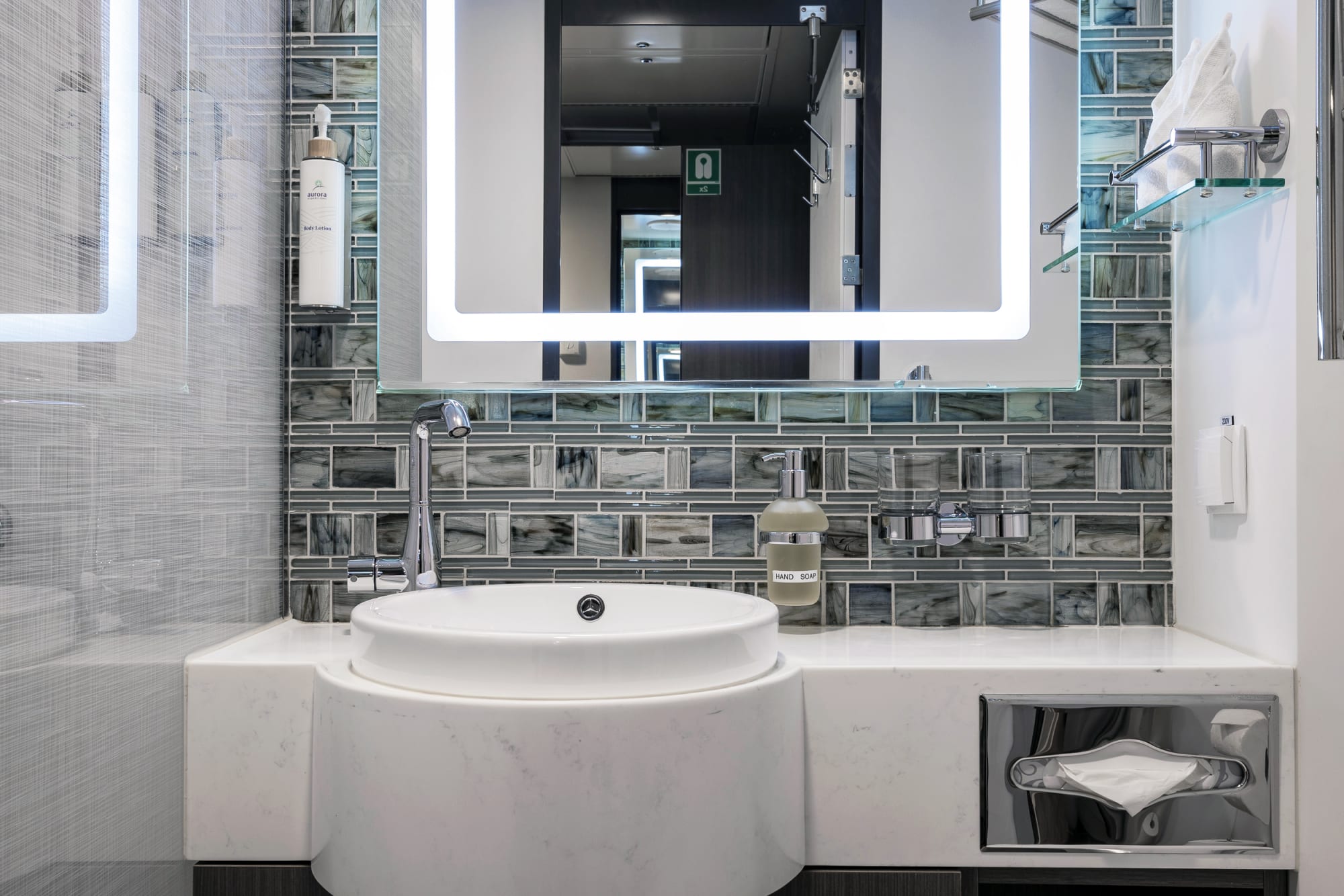 A contemporary bathroom aboard a cruise ship featuring a sleek white marble vanity with