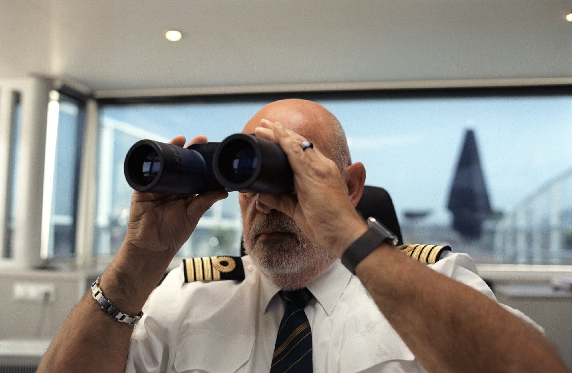 A senior captain in white uniform shirt and black tie, wearing officer's insignia on his sleeves