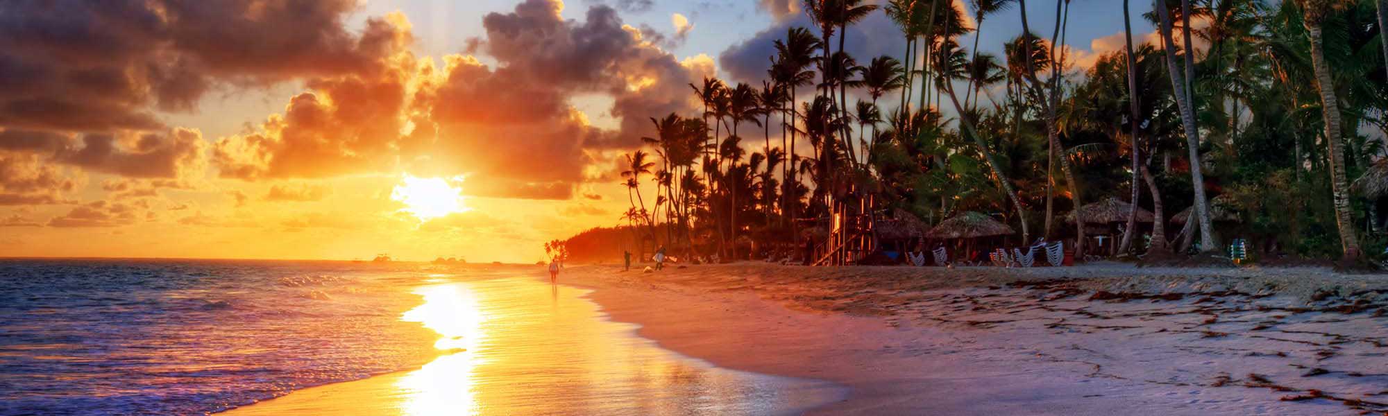 A stunning tropical sunset over a pristine beach lined with tall palm trees and traditional