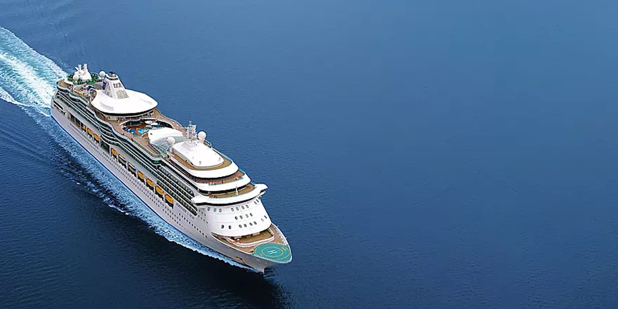 An aerial view of a large modern cruise ship with multiple white decks and golden trim sailing