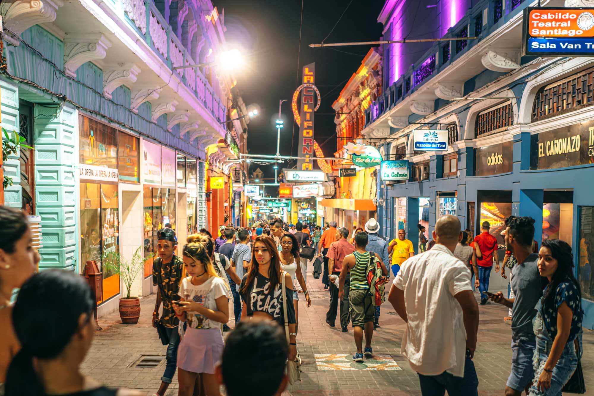 A vibrant nighttime street scene in Santiago de Cuba filled with locals and shoppers beneath