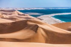 Dramatic aerial view of massive golden sand dunes adjacent to a pristine turquoise ocean and white