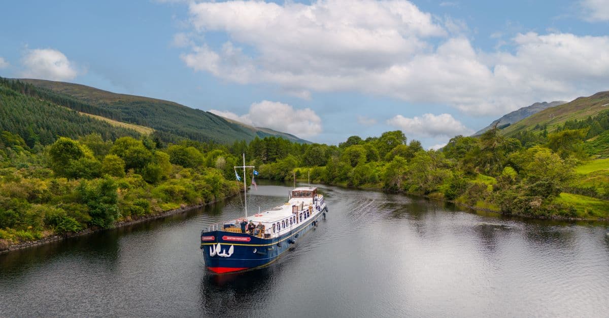 A picturesque river cruise vessel navigates through calm waters surrounded by lush green mountains