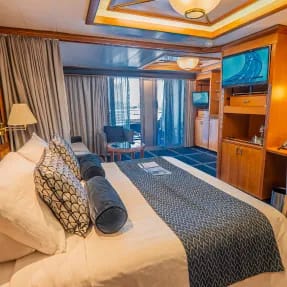 An elegantly appointed cruise ship stateroom featuring a king bed with decorative pillows