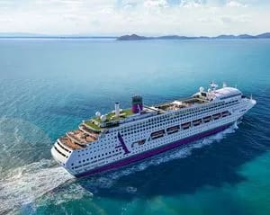 A large modern cruise ship navigates crystal-clear turquoise waters near a tropical island