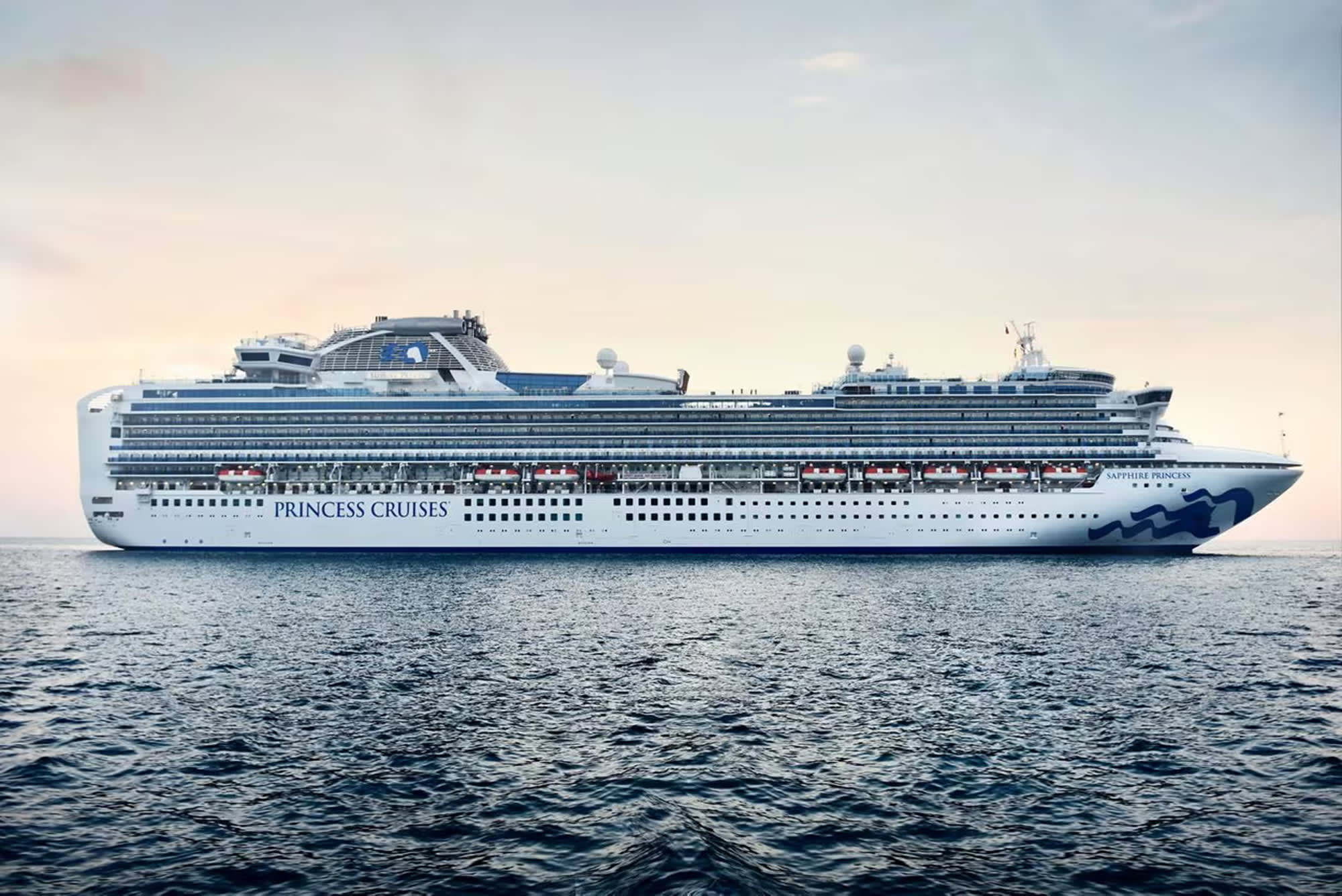 A large white and blue Princess Cruises ocean liner sailing on a serene, rippled seascape during