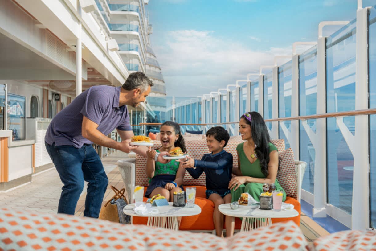A joyful family of four dines together on an open-air deck aboard a Princess Cruises ship, with