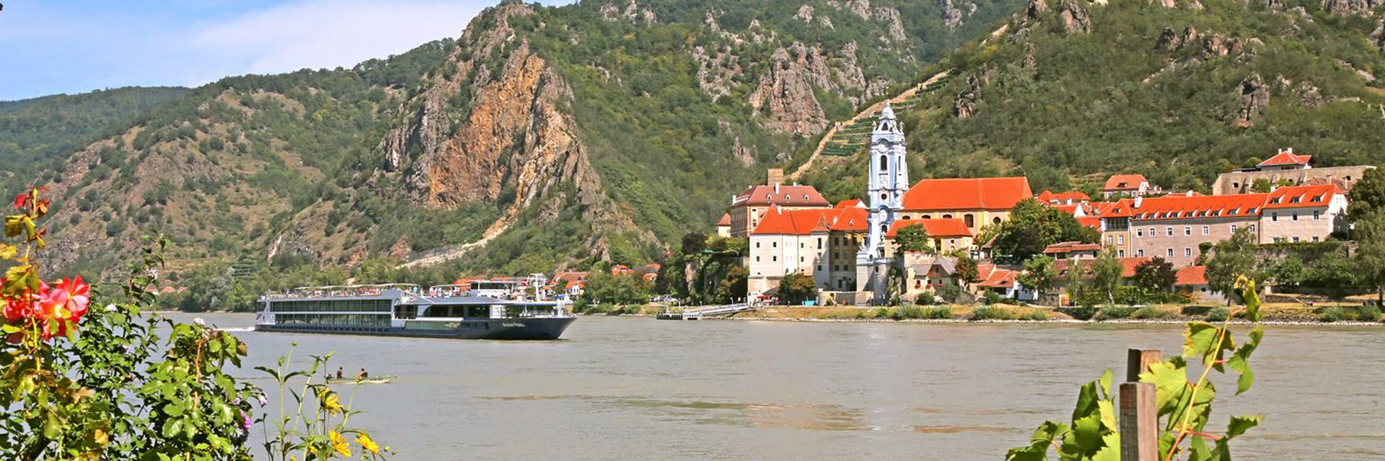 A river cruise ship navigates the Danube River past a picturesque riverside village nestled beneath