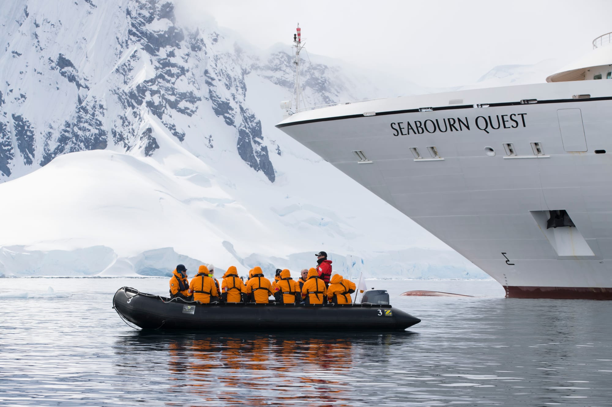Passengers in a black Zodiac inflatable boat wearing bright orange life jackets prepare for