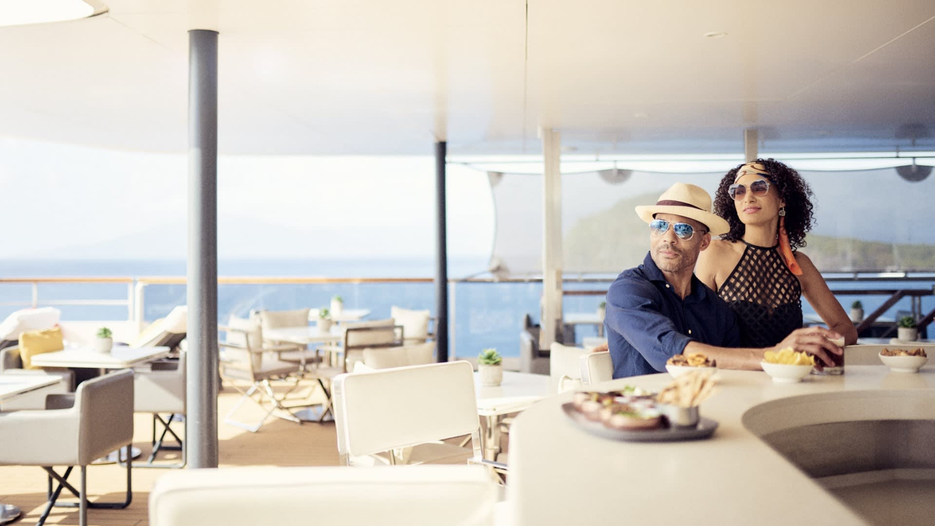 A well-dressed couple enjoys a meal on an expansive outdoor deck of a luxury yacht, with panoramic