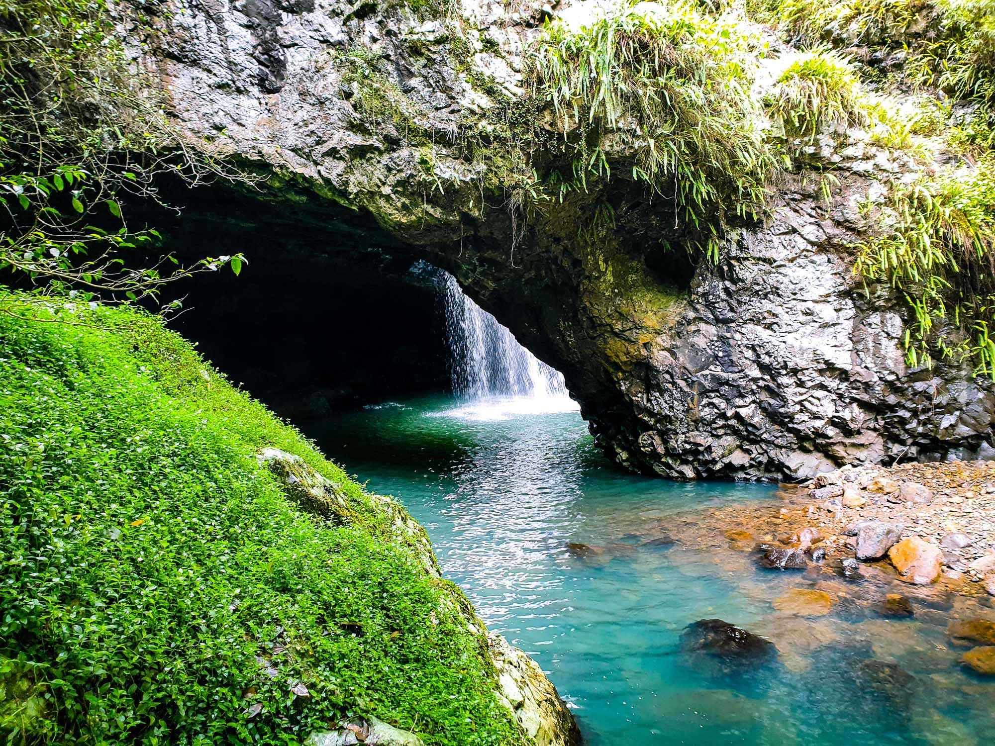 A stunning natural cave formation features a cascading waterfall flowing into a pristine turquoise