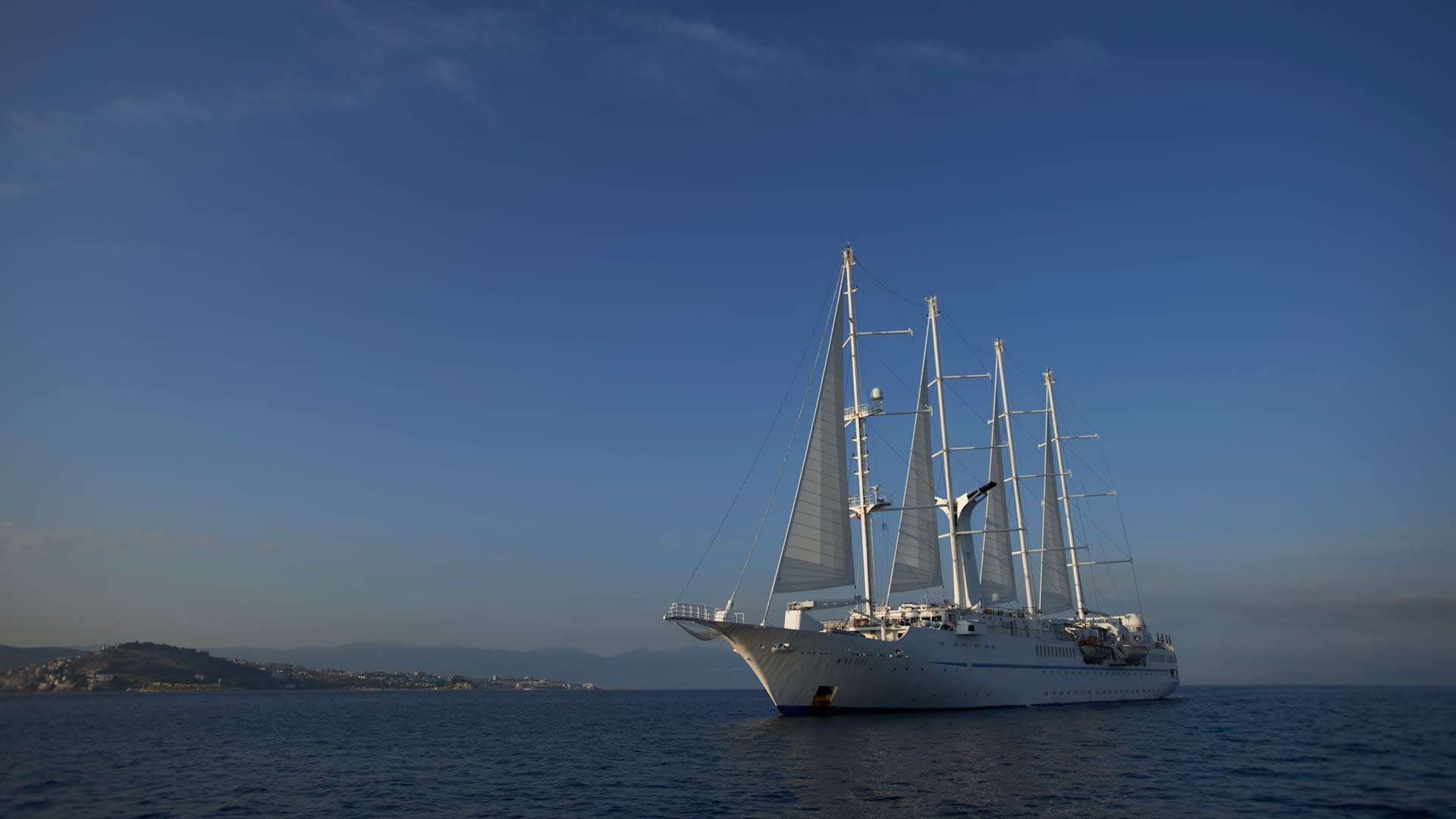 A striking white multi-masted sailing ship anchored in clear blue Mediterranean waters, with