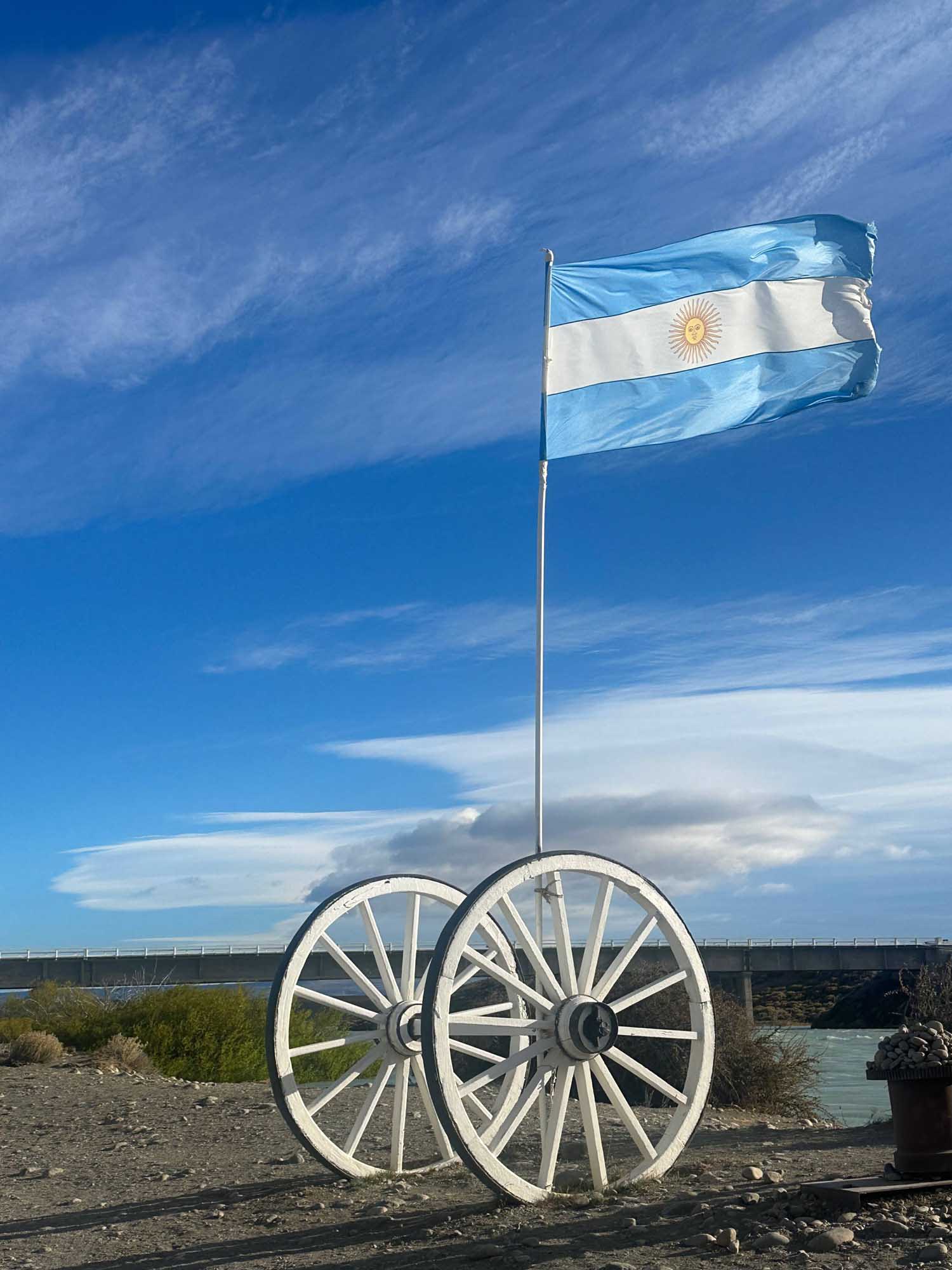 The Argentine flag flies proudly from a flagpole mounted on a pair of white wooden wagon wheels